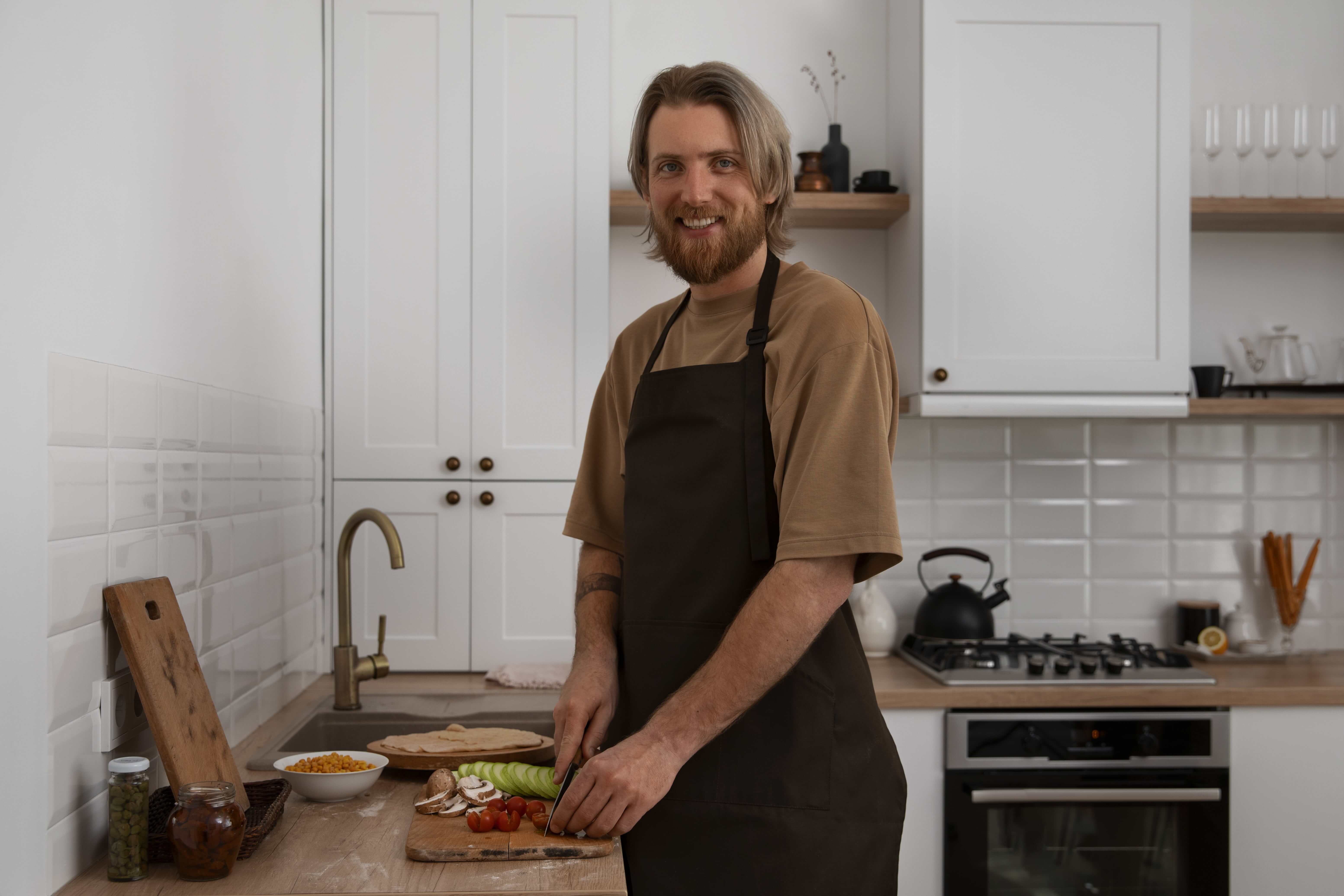 In a modern kitchen, a man in an apron is chopping fresh vegetables, demonstrating his cooking expertise.